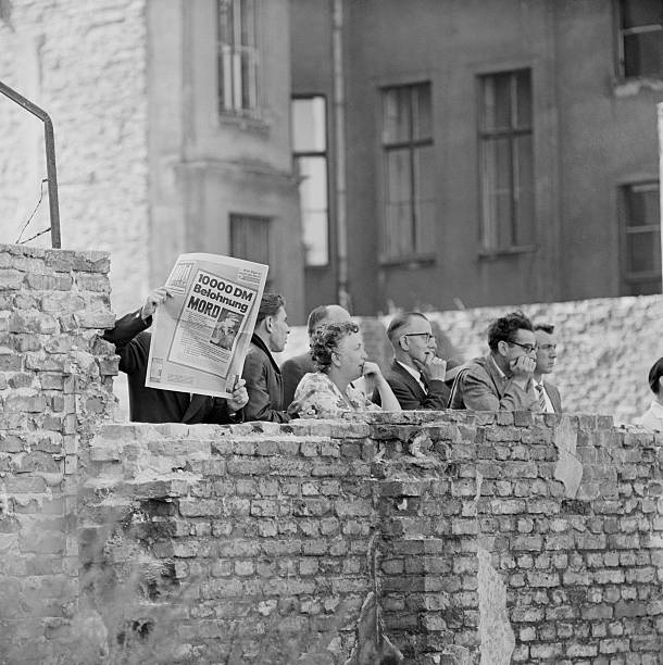 (Original Caption) 9/4/1961-Berlin, Germany- One group of West Berliners peering over sector wall here recently holds up special edition of German newspaper which offers 10,000-mark reward for information on East German policeman who shot and killed a refugee trying to swim to freedom across a canal Aug. 29. The caption, with photo, on front page says "This is the murderer." The paper states, however, the slayer's name is still unknown.